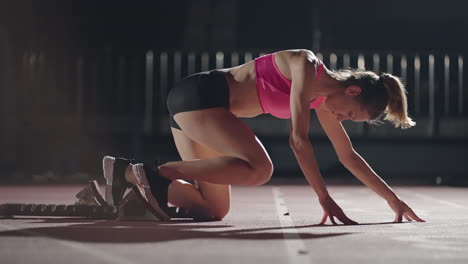 Fit-mixed-race-female-athlete-on-a-running-track-at-an-outdoor-sports-stadium-starting-a-race-from-starting-blocks-in-slow-motion-backlit-with-lens-flare.-Night